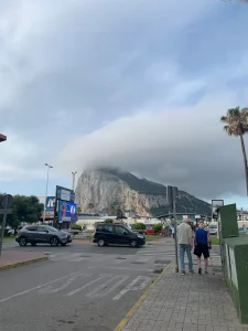 Pedestrians walking away towards the frontier, the Rock of Gibraltar under a cloud cap.