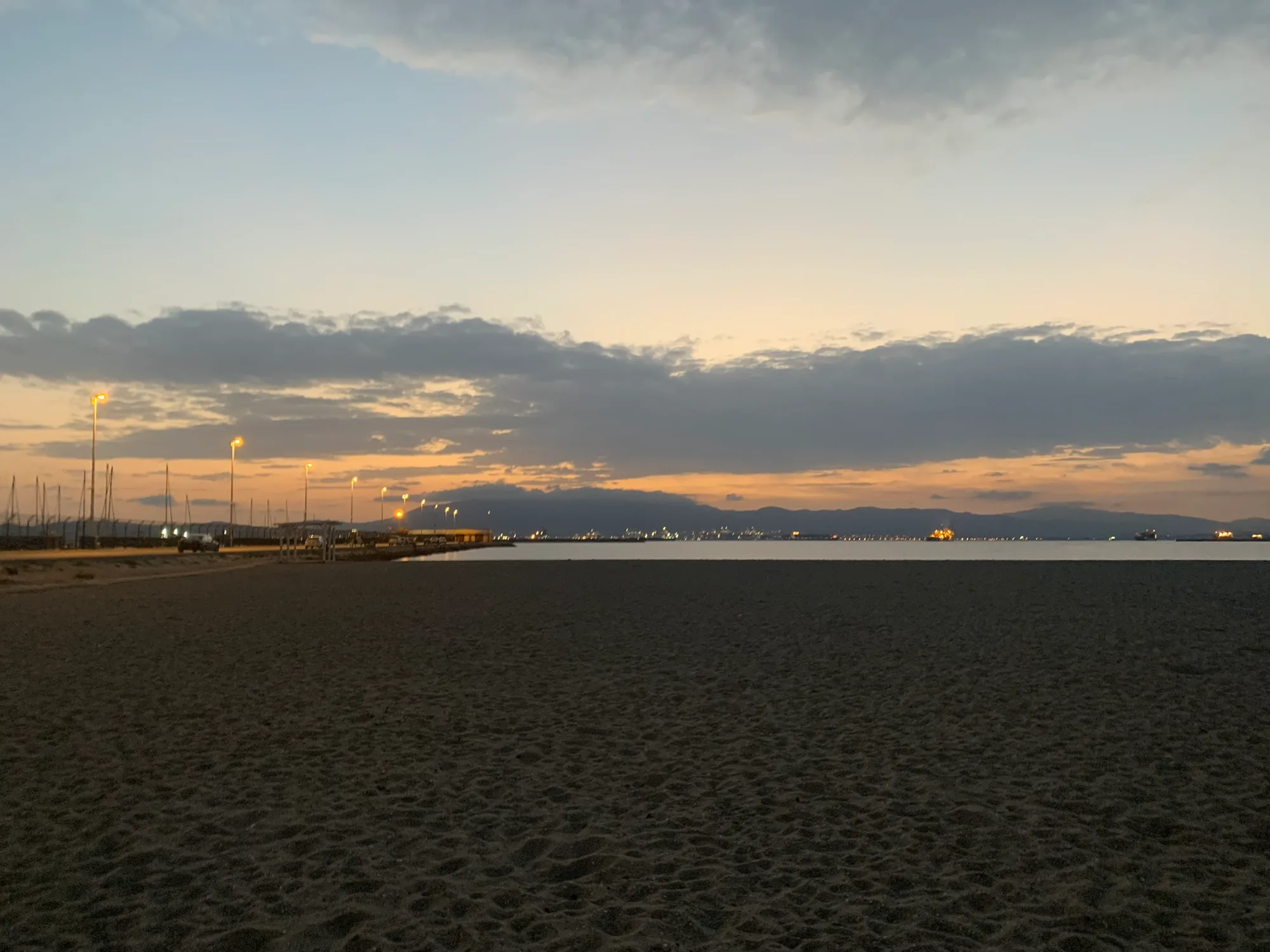 Sunset over the bay at La Atunara, masts of moored boats in the foreground.
