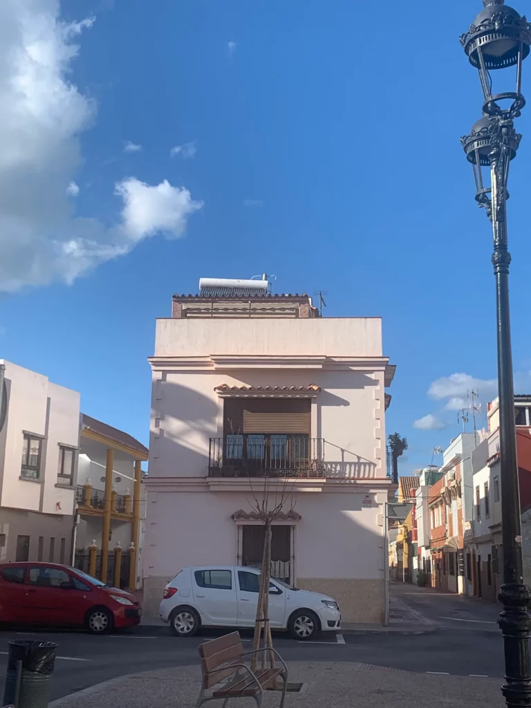 A corner house in La Linea with a wrought-iron balcony and a street lamp.