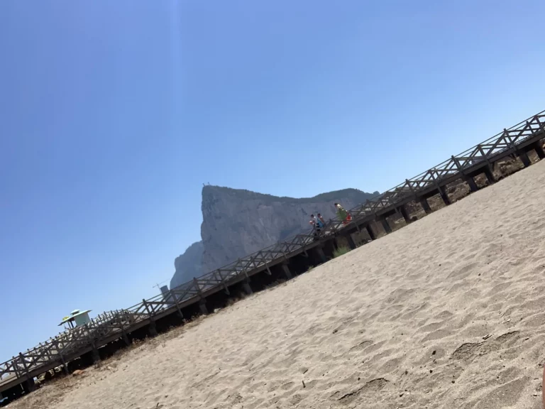Walkers on the Playa de Levante boardwalk, the Rock of Gibraltar ahead of them.