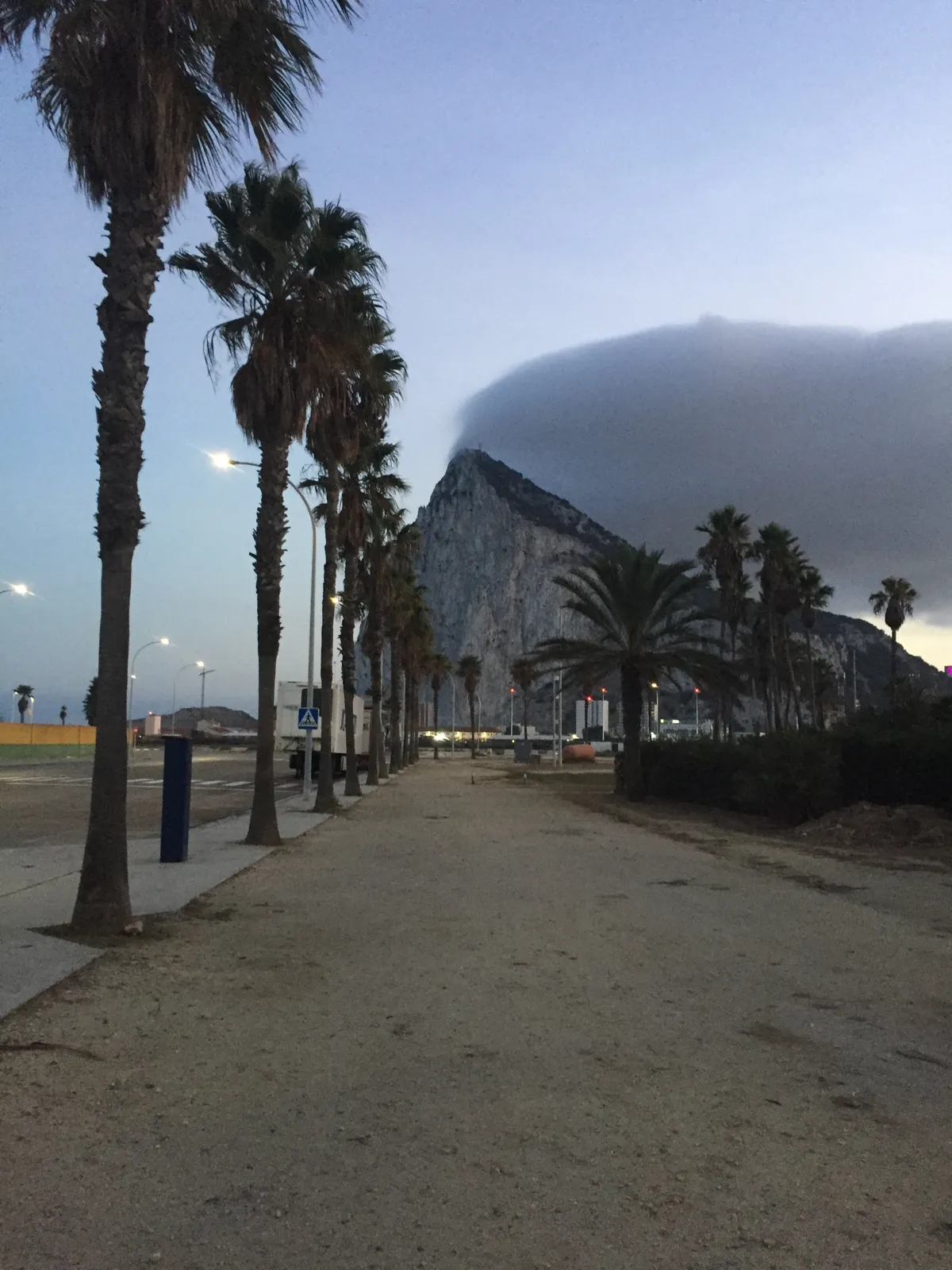 A palm-lined promenade in La Línea with the Rock of Gibraltar under cloud at dusk